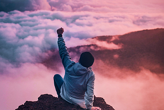 Man sitting on cliff with a fist bump in the air