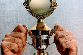 Two hands holding a tiny trophy that barely fits around his fingers