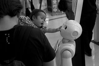 a baby interacting with Pepper the robot, taken from https://www.flickr.com/photos/jeena/37017614286/