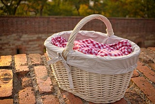 A wicker basket with a red checked gingham cloth, ready to be picked up and carried.