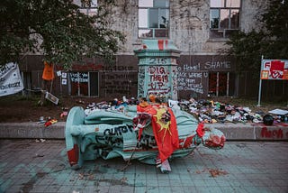 A statue of Egerton Ryerson is on the ground. Behind it, its base is covered in graffitti that says, “Dig them up” and more. The base of the statue is surrounded in children’s shoes to commemorate 215 Indigenous children found buried in an unmarked mass grave at the site of Kamloops Indian Residential School.