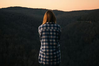 Woman wearing blue and white plaid dress shirt in front of green mountain.