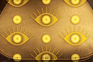 Simple gold handbag with two styles of bright gold “evil” eyes superimposed in a geometric pattern.