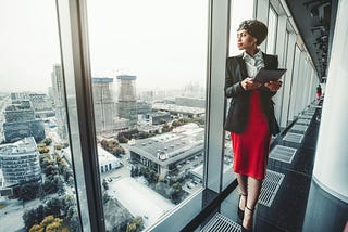 A woman looks out of a skyscraper window at the skyline.