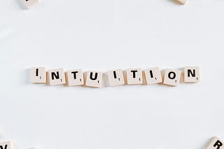 “Word ‘intuition’ spelled out with Scrabble tiles on a white background.”