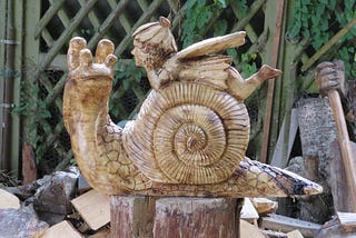 A carved wood snail and tiny fairy on its shell.