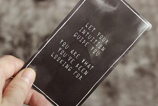 A hard hold a black card with white writing that reads, “Let your intuition guide you. You are what you’ve been looking for.”