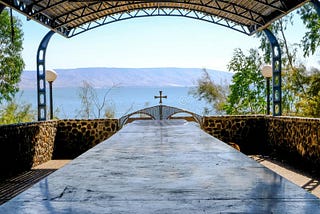 long table under a metal roof with a low gate with a cross leading into lake Galille