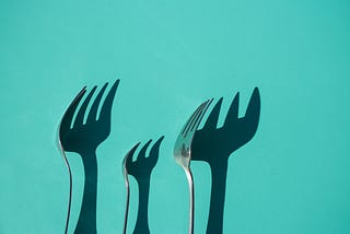 Forks make shadows on a green wall.