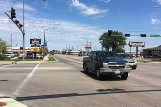 Photo of 4-lane street with restaurants and auto retailers.