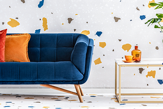 Royal blue MidCentury Modern couch with peg les sitting in front of a confetti colored wall.