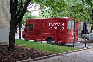 A photo of the Tartan Express food truck. It is red, labeled with TARTAN EXPRESS and “delicious” in various languages.