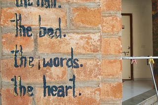 Painted Inscription on a wall of red bricks — It’s All Messy. The Bed. The Words. The Heart. Life.