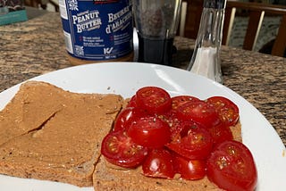 An open peanut butter tomato sandwich featuring the ingredients in the background.