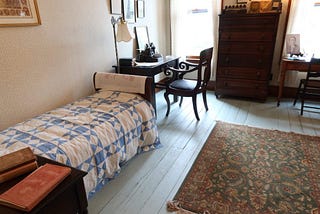 Room with small bed and writing table with old manual typewriter.