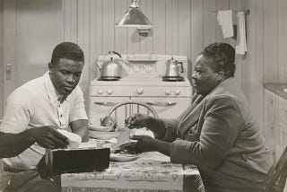 Jackie Robinson sitting at a table in a scene from a movie where he played himself in “The Jackie Robinson Story” (1950).