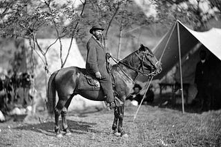 Allan Pinkerton, founder of the Pinkerton Detective Agency, on horseback beside some Civil War era tends.
