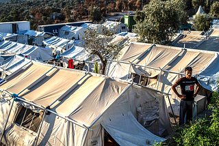 A man standing in front of a series of aid tents set up for refugees spilling out of Camp Moria.