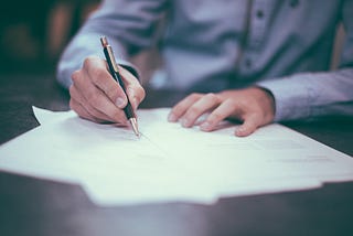 A man wearing professional attire, writing on a résumé with a pen