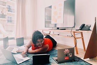 Woman sitting in front of 5 laptops in front of a large TV