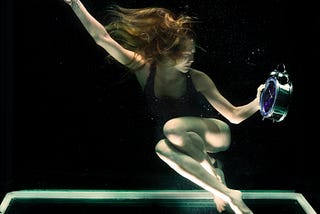 Woman underwater in a black bathing suit holding a clock.