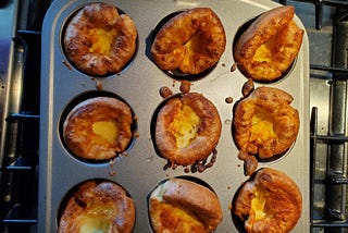 A muffin tin showing nine golden brown, cooked Yorkshire Puddings.