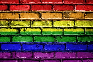 image of a brick wall that seemingly has the colors of the LGBTQ+ rainbow flag painted on it