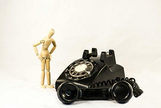An old black rotary dial phone with the receiver off hook beside beige manekin.