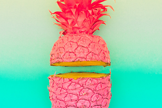 A pineapple that’s been spray-painted hot pink and sliced open against a bright blue background.