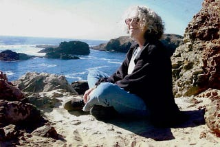 photo of woman smiling in the sun, sitting on a beach with the sea behind