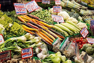Photo of brightly colored vegetables, including orange carrots, red tomatoes, and green onions, at Sosio’s Fruit and Produce Stand, Pike Place Market, Seattle