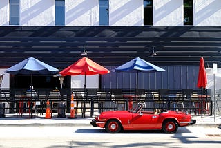 red convertible in front of outdoor seating with red and blue umbrellas