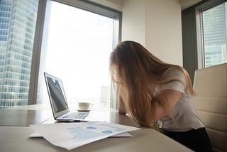 mulher sentada em seu escritório, na frente de um notebook, com as mãos no rosto, expressando a frustração.