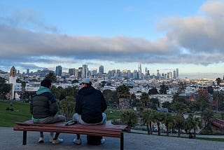 2 people sitting on a bench looking over Dolores park and downtown San Francisco