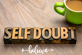A cup of coffee next to a piece of wood labeled ‘Self Doubt,’ with the word ‘Believe’ written in a graphic style below it