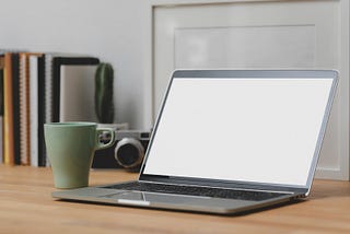 Laptop with blank screen on a desk beside a cup of coffee.