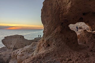 Stone arch by the ocean and sun is setting.