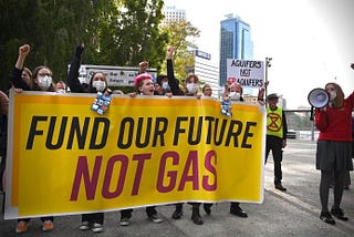 5 students holding a yellow banner that reads: Fund our future, Not gas. Also a student to right holding a megaphone.