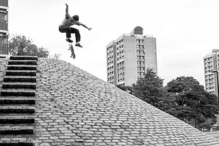 Skater does a flip-trick over a cobbled bank.