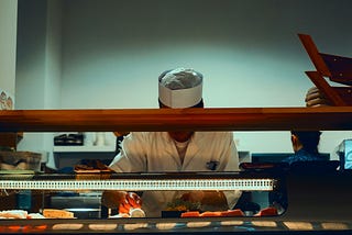 A cook assembling a sandwich with their face hidden behind a counter