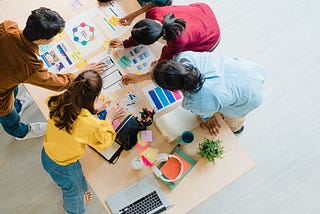 An image of male and female colleagues huddled around a table critiquing each others work.