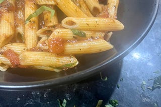 A picture of the pasta served in a bowl, penne in a tomato sauce with some shredded basil thrown overtop.