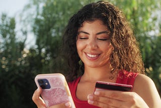 Young African American woman using cell phone holding credit card online shopping. Hispanic female shopper using instant easy mobile payments making purchase in online store. E-banking app service.