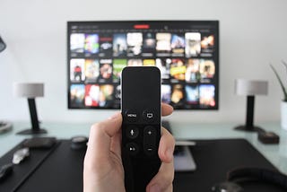 A hand holding a TV remote while watching shows on a streaming service on Television.