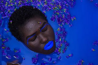 Anthropology in the News. Ancient chewing gum discovery. Image: Black woman in blue water with blue eye and lip makeup.