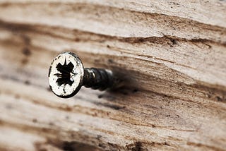 Screw head coming out of a piece of wood.