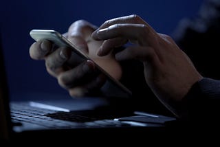 Close up of white person’s hands typing on a phone in ominous darkness