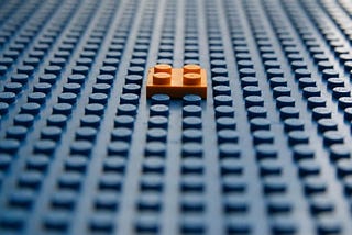 Single orange lego piece stuck in the middle of a blue lego board.