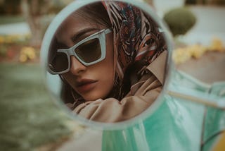 image of a woman looking at herself through a car’s side mirror. Photo credit: Lance Reis, Unsplash