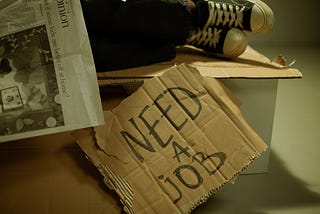 A cardboard sign saying “NEED A JOB”